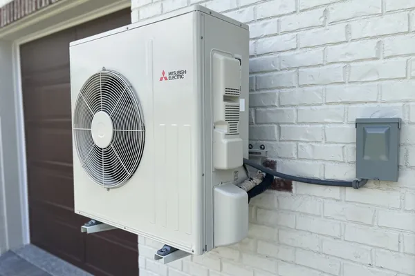 A Mitsubishi ductless condenser mounted on a white brick wall