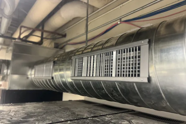 Exposed spiral ductwork with a supply grille above a commercial interior