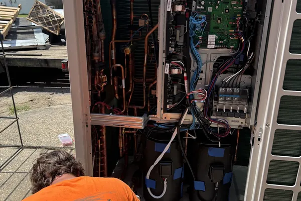 A Climatech technician working inside an open outdoor unit