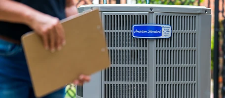 Technician holding a clipboard beside an American Standard Platinum Series air conditioner