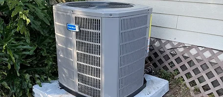 American Standard air conditioner condenser unit on a concrete pad beside a home