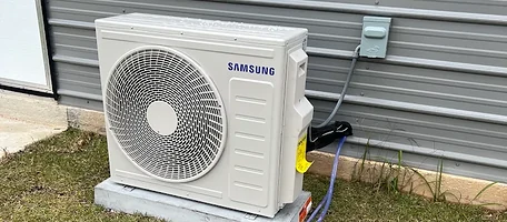 Samsung ductless mini split outdoor unit on a concrete pad beside metal siding