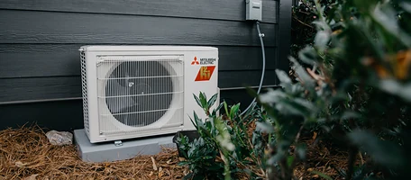 Mitsubishi Electric ductless heat pump outdoor unit installed on a pad beside a home