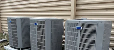 Three American Standard condenser units installed side by side on concrete pads