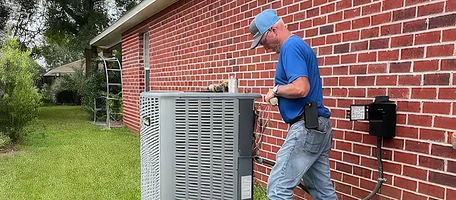 HVAC technician servicing an outdoor unit at the electrical disconnect of a brick home